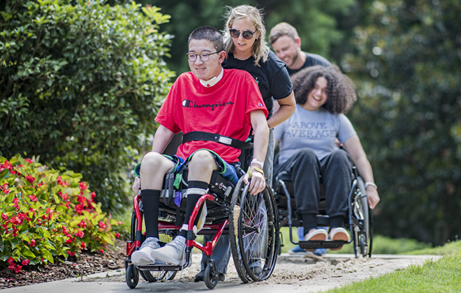 Patient with a spinal cord injury using a wheelchair and being pushing by a therapist on a nature trail